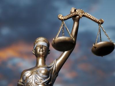 Vrouwe Justitia beeldhouwwerk met weegschaal tegen een achtergrond van een dramatische lucht.