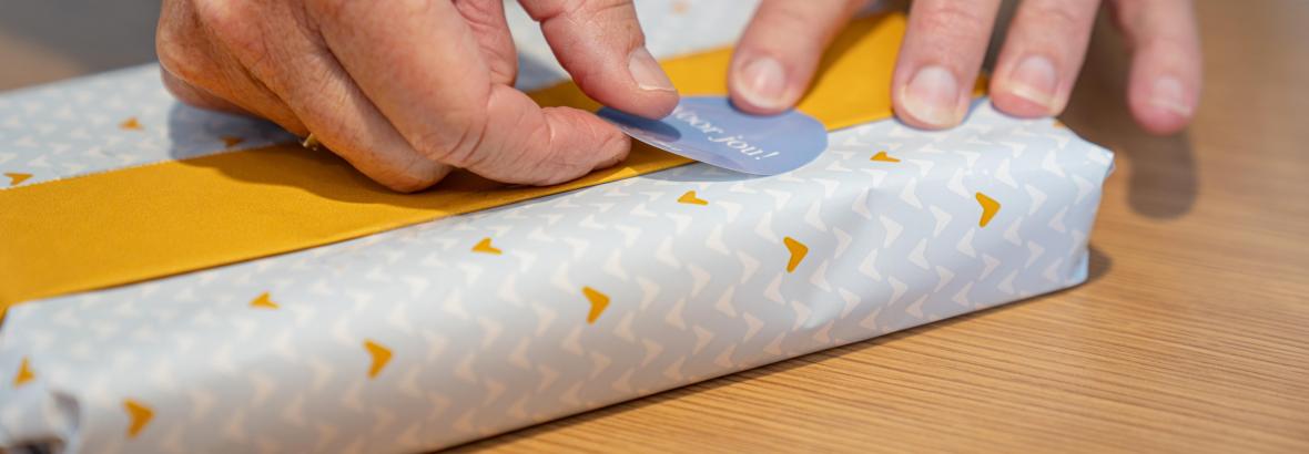 Handen wikkelen cadeautje in met cadeaupapier en geel lint en voegen sticker toe.