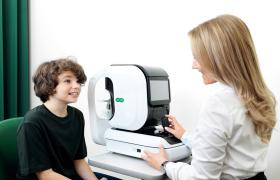 Opticien voert een oogmeting uit bij een kind met behulp van een apparaat in een Specsavers-winkel.