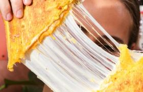 Een tosti wordt uit elkaar getrokken met smeltende kaas zichtbaar op de achtergrond van een koffiehuis.