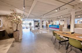 Interieur van een sanitairwinkel met showroom, tafels en decoratieve elementen zoals een kunstboom en vloertegels.