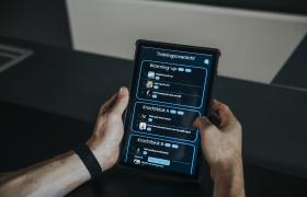 Twee handen houden een tablet vast met een trainingsoverzicht van een sportschool-app op het scherm.