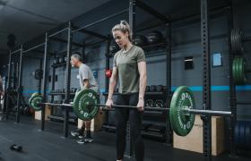 Mensen tillen halters in een moderne fitnessruimte met gewichthefracks en trainingsapparatuur op de achtergrond.