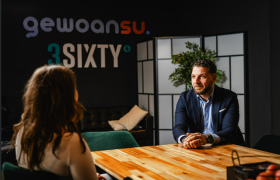 Twee mensen in gesprek aan een houten tafel in een modern kantoor met de woorden gewoansu. 3SIXTY op de achtergrond.