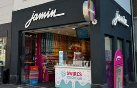 Voorgevel van een Jamin winkel op een hoek met een Swirl's Ice Cream balie en wanden vol gekleurd snoepgoed.